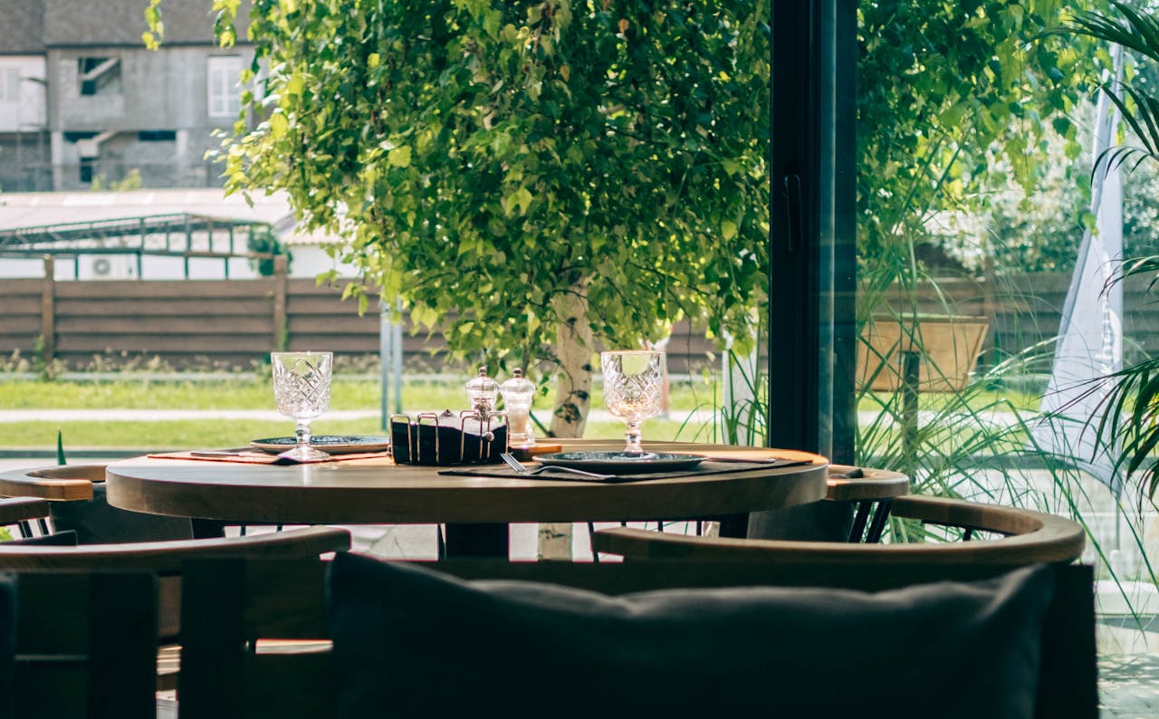 Inviting restaurant table set beside large windows with lush outdoor greenery lighting up the space.